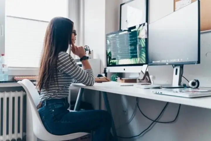 Jugendliche programmiert am Schreibtisch mit zwei Monitoren